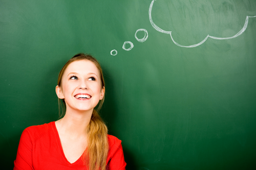 Woman standing in front of blackboard with thought bubbles drawn on it