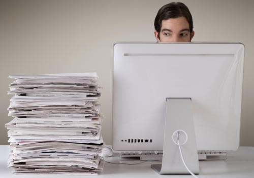 Man sitting at his computer with a pile of documents next to him